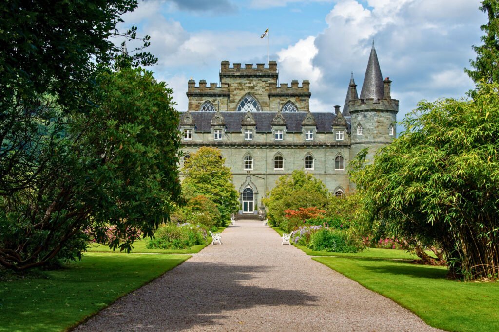 Tree-lined pathway leading to the grand Gothic Revival facade of Inveraray Castle, surrounded by lush gardens in Scotland