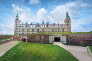 Panoramic view of Kronborg Castle above moat and gate in Helsingør, Denmark, under blue sky with clouds.