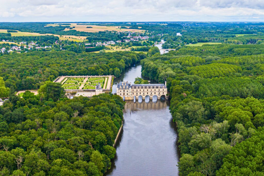 Aerial view of Château de Chenonceau spanning the Cher River, surrounded by formal gardens and dense forest in the Loire Valley, France