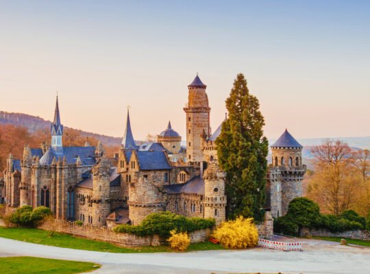 Löwenburg Castle in Kassel, Germany, framed by early spring foliage and soft sunset light, showcasing its Romantic-style turrets and towers.