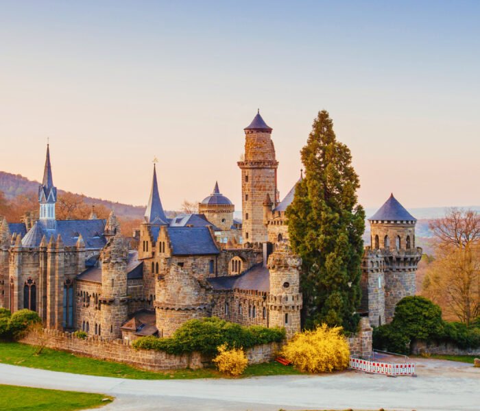 Löwenburg Castle in Kassel, Germany, framed by early spring foliage and soft sunset light, showcasing its Romantic-style turrets and towers.