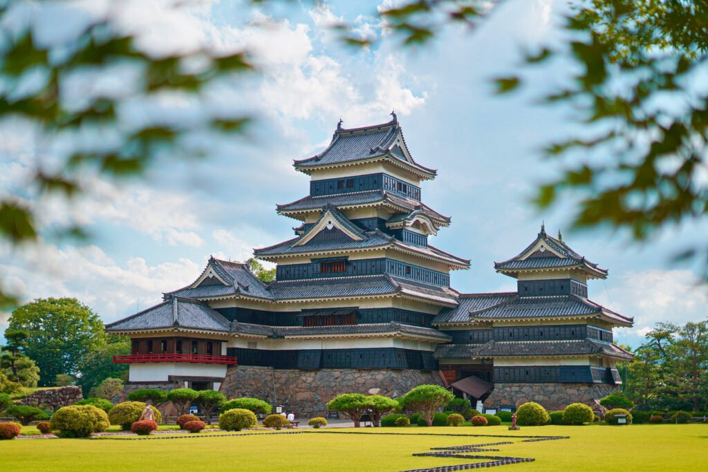 Front view of Matsumoto Castle with well-manicured gardens and summer greenery under a bright blue sky in Nagano Prefecture, Japan.
