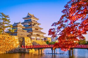 Matsumoto Castle by red bridge and autumn leaves at sunset in Japan