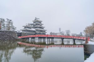 Snowy Matsumoto Castle and red bridge in Japan, serene water reflection