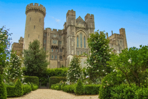 Arundel Castle rising above formal rose gardens under a clear blue sky in West Sussex, England.