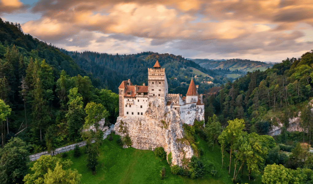 Aerial view of Bran Castle at sunset, perched on a rocky hill and surrounded by forest in Transylvania, Romania.