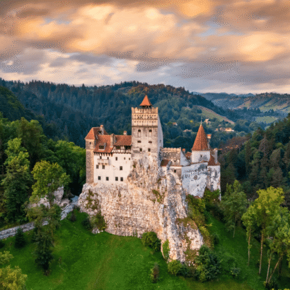 Aerial view of Bran Castle at sunset, perched on a rocky hill and surrounded by forest in Transylvania, Romania.