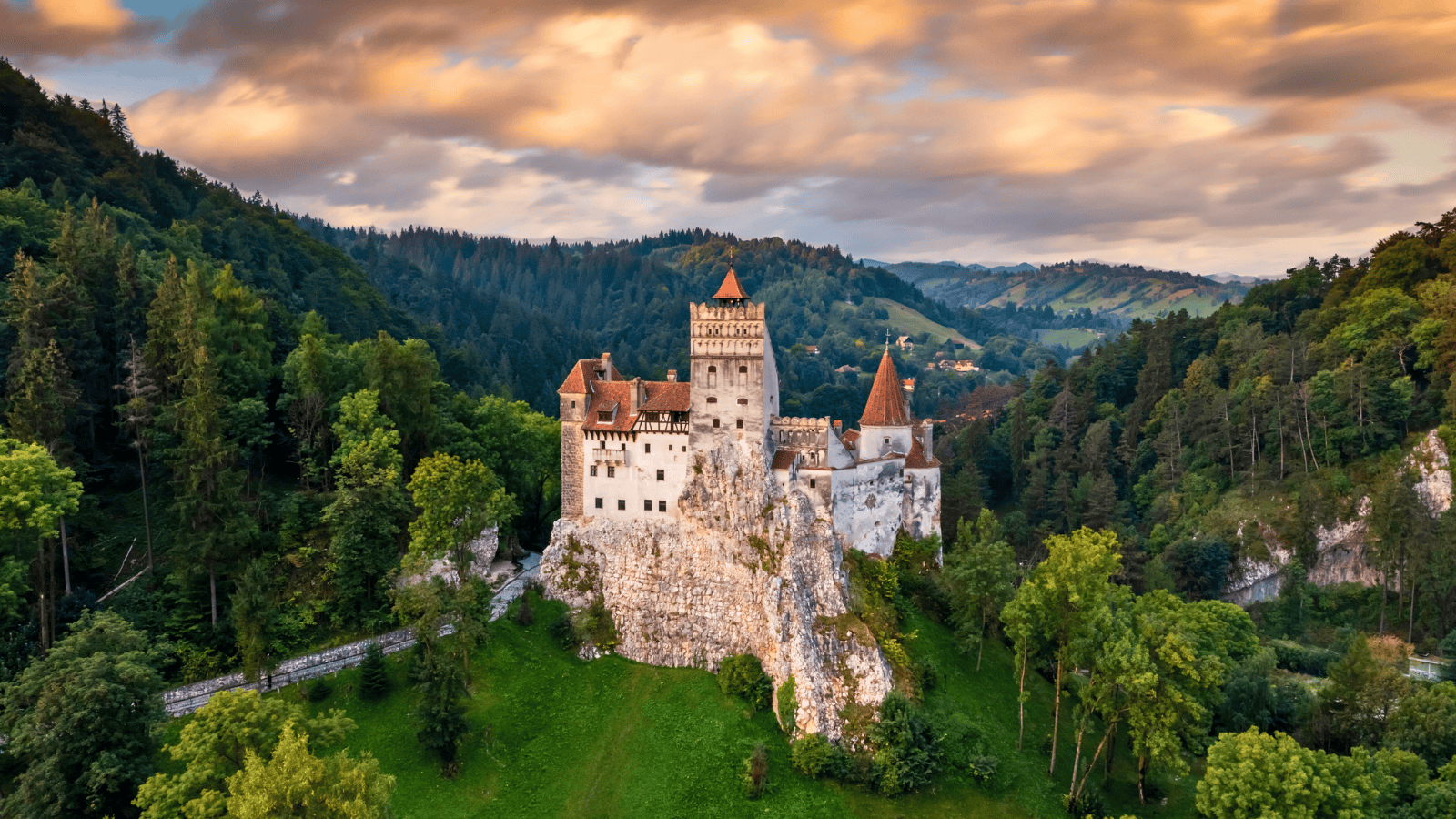 Aerial view of Bran Castle at sunset, perched on a rocky hill and surrounded by forest in Transylvania, Romania.