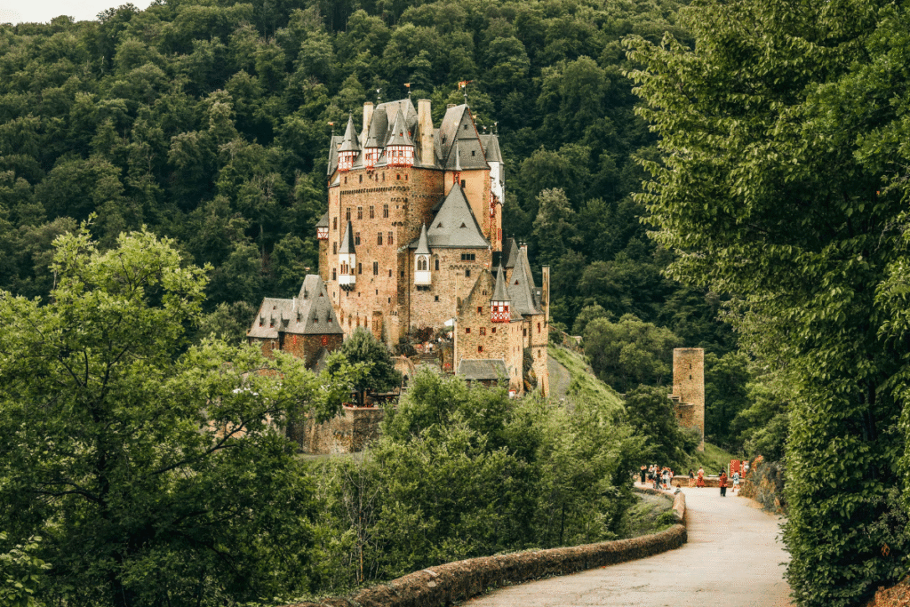 Burg Eltz nestled in a green forest, with visitors approaching along a winding path in Germany.
