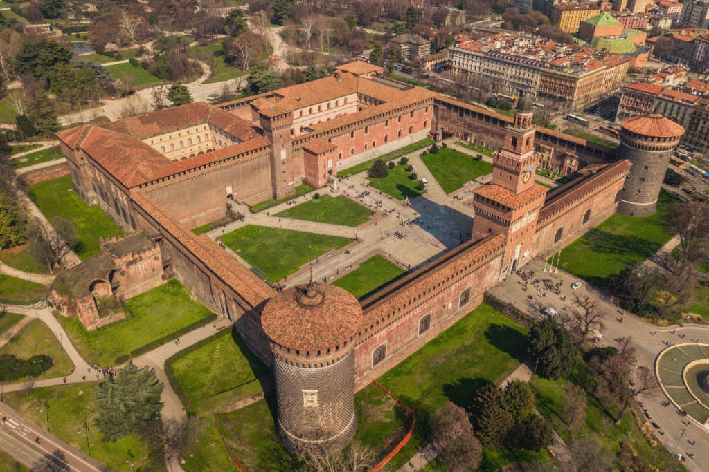 Aerial view of Castello Sforzesco in Milan, Italy, showing its square layout, towers, and central courtyard surrounded by city and parkland.