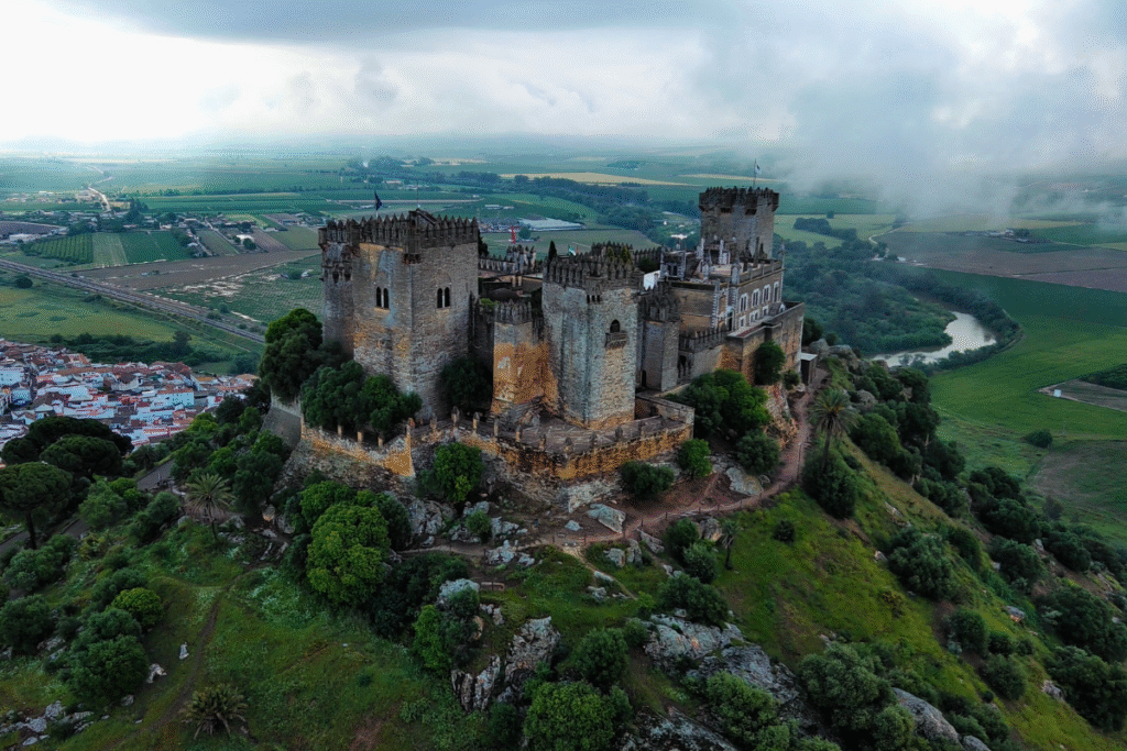 Aerial view of Castillo de Almodóvar del Río on a lush green hilltop in Spain, surrounded by farmland and village