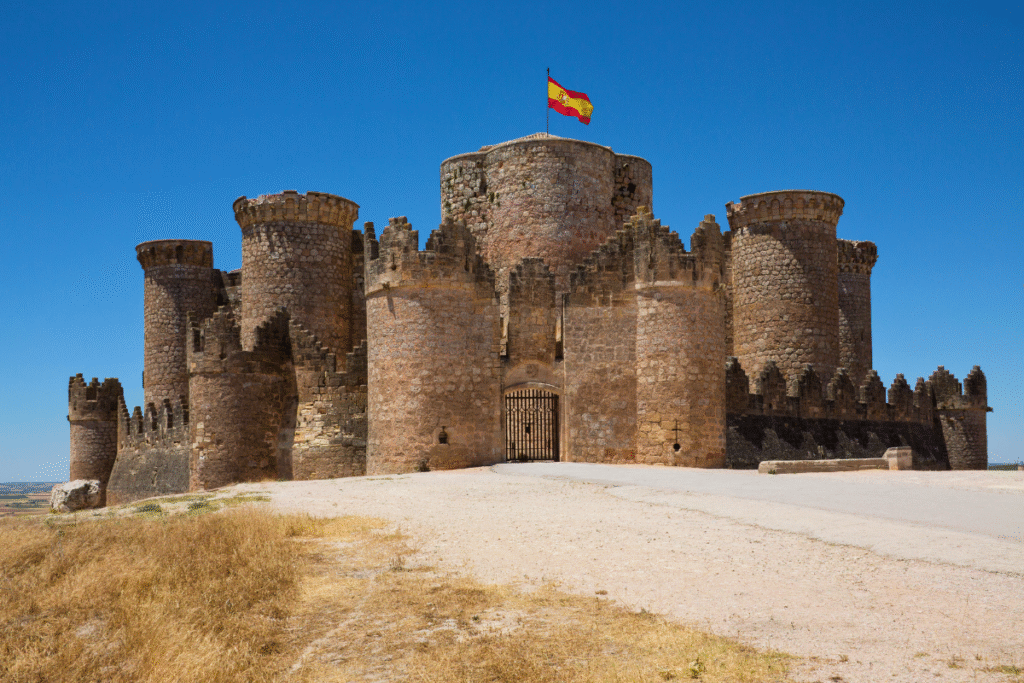 Castillo de Belmonte with its star-shaped stone towers and the Spanish flag flying above, set against a clear blue sky