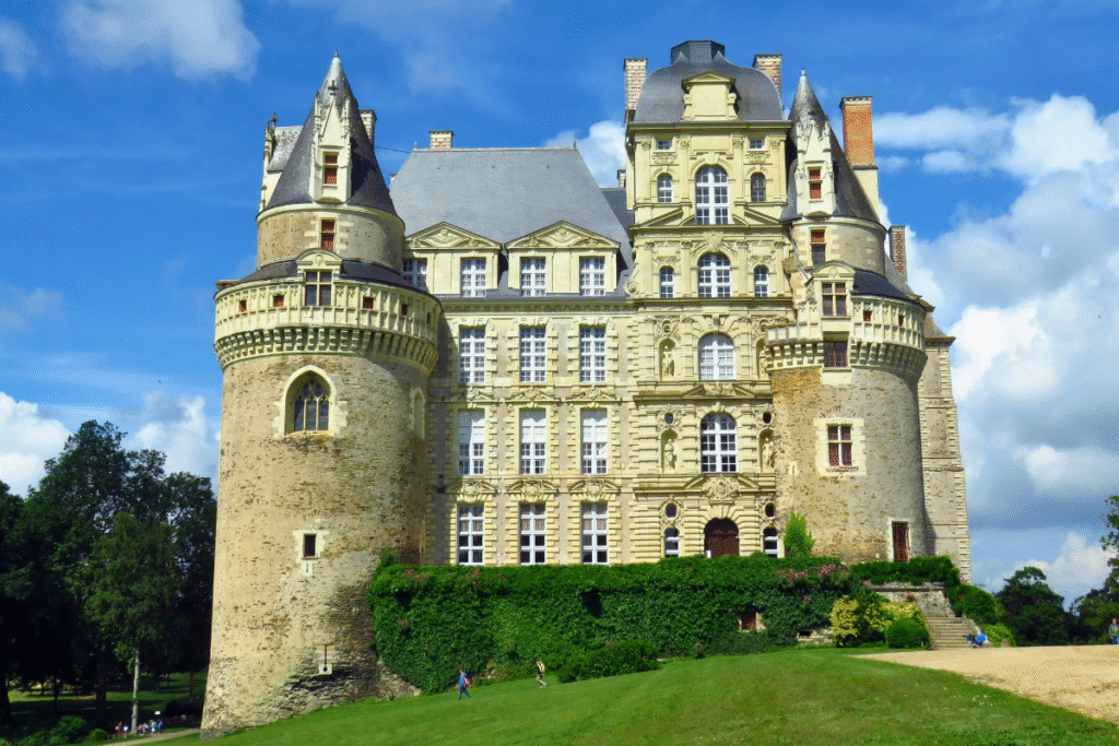 Front view of Château de Brissac in France, showing its elegant towers, ornate windows, and lush green surroundings on a sunny day.