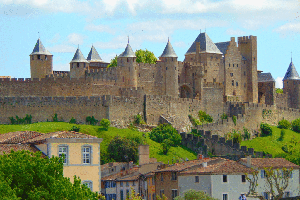 The fortified medieval walls and towers of Château de Carcassonne rising above the rooftops of the town on a sunny day.