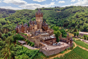Aerial view of Reichsburg Cochem, a hilltop castle surrounded by green forests and vineyards in the Moselle Valley, Germany.