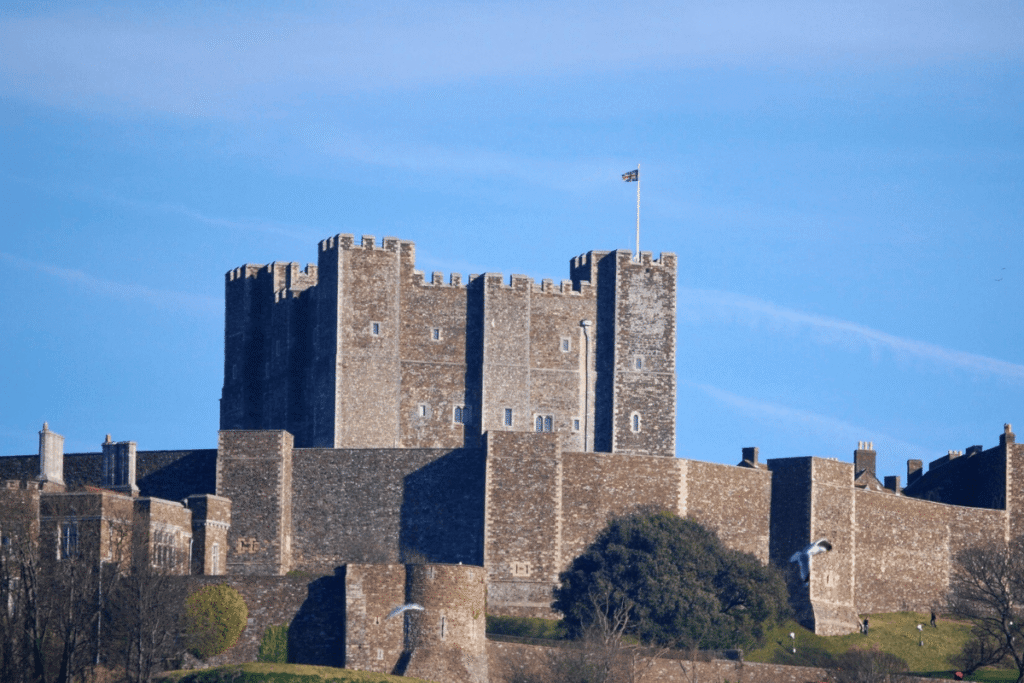 Dover Castle’s stone Great Tower and defensive walls rise above the green hillside under a clear blue sky.