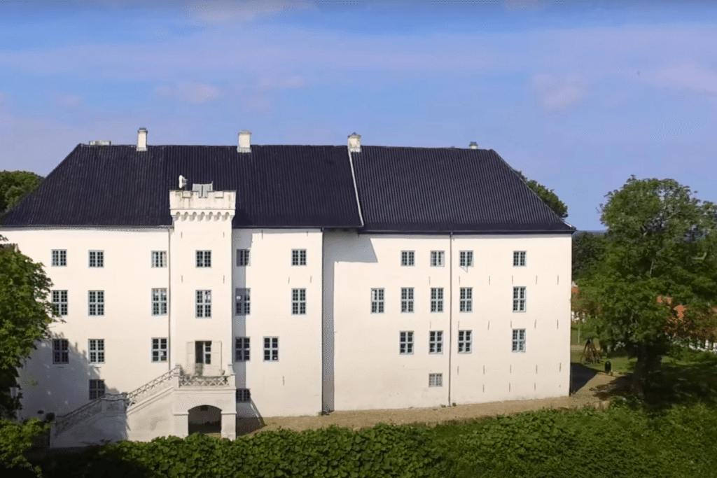 Front view of Dragsholm Castle in Denmark, with its bright white walls and black roof, surrounded by green trees on a clear day.