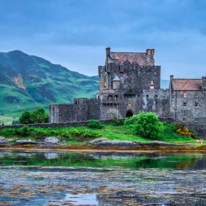 Castelo de Eilean Donan sob céu nublado, cercado por água e montanhas das Highlands escocesas.