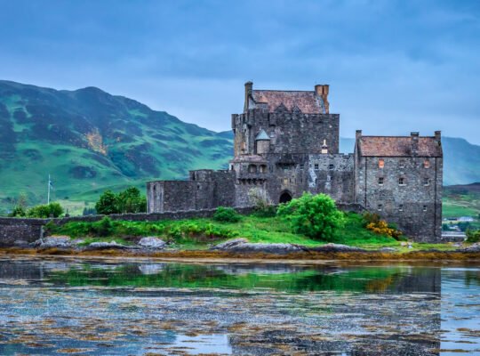 Castelo de Eilean Donan sob céu nublado, cercado por água e montanhas das Highlands escocesas.