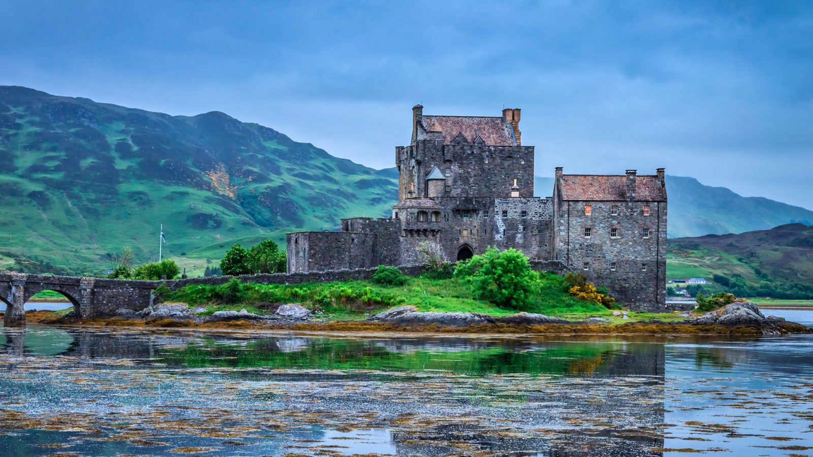 Castelo de Eilean Donan sob céu nublado, cercado por água e montanhas das Highlands escocesas.
