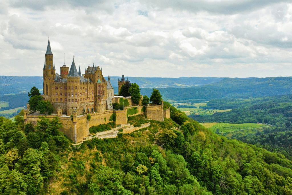 Aerial view of Hohenzollern Castle perched on a forested hilltop, surrounded by rolling green hills in Baden-Württemberg, Germany.