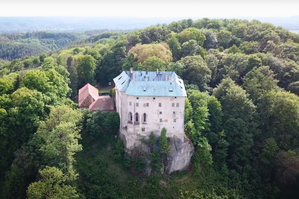 Aerial view of Houska Castle in the Czech Republic, perched on a rocky outcrop and surrounded by dense green forest.