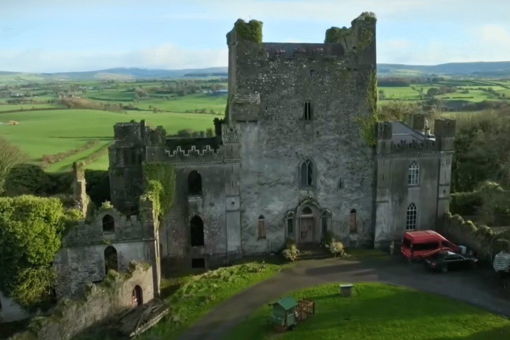 Front view of Leap Castle, Ireland, with its rugged stone walls and ivy-covered ruins set against rolling green countryside.