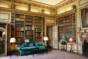 Interior of Leeds Castle library with tall bookshelves, velvet sofa, and lamps