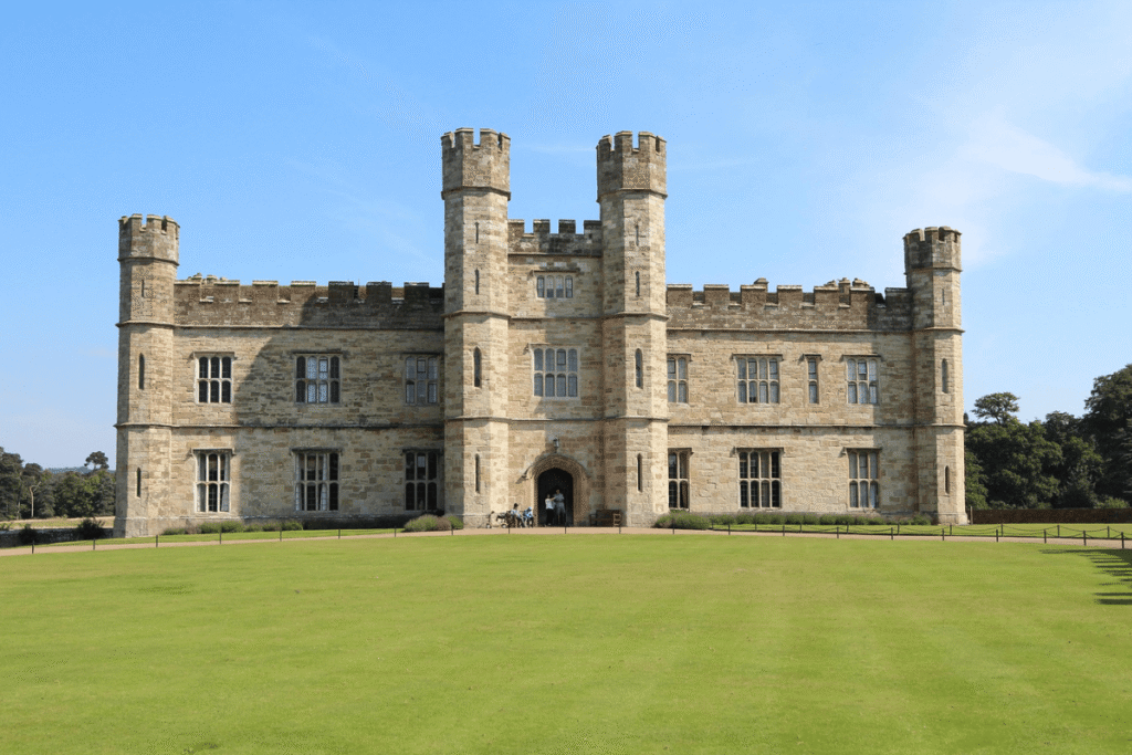 Front view of Leeds Castle, with its historic stone façade and green lawn under a clear blue sky.