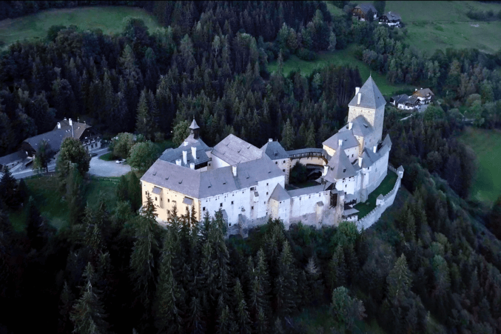 Aerial view of Moosham Castle in Austria, surrounded by dense forest and rolling green meadows at dusk.