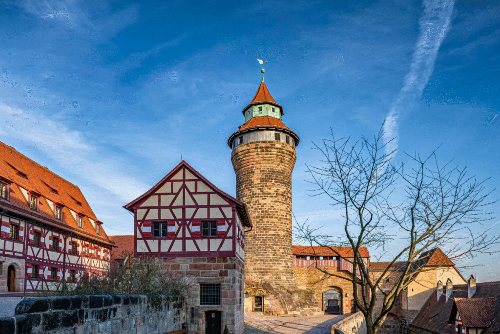 Half-timbered buildings and the Sinwell Tower inside Nuremberg Castle under a clear blue sky.