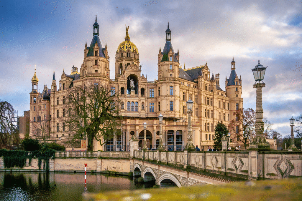 Schwerin Castle reflected in the water, with ornate towers and a golden dome under a dramatic sky in northern Germany.