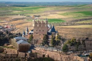 Alcázar of Segovia castle rises above the Spanish countryside on a sunny spring day.