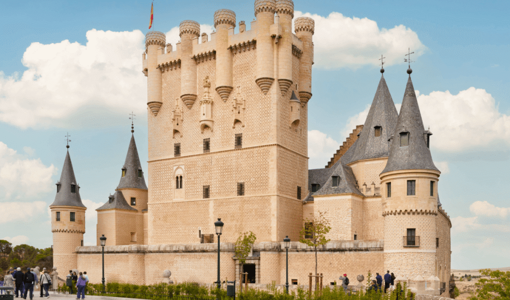 People walking by the Alcázar of Segovia castle under a blue sky.