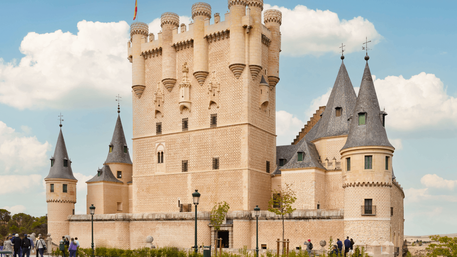 Alcázar of Segovia castle in Spain with tourists, distinctive turrets under blue sky.