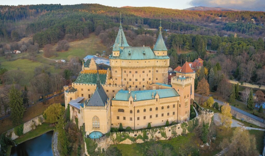 Aerial view of Bojnice Castle surrounded by autumn forests in Slovakia, medieval architecture is visible.