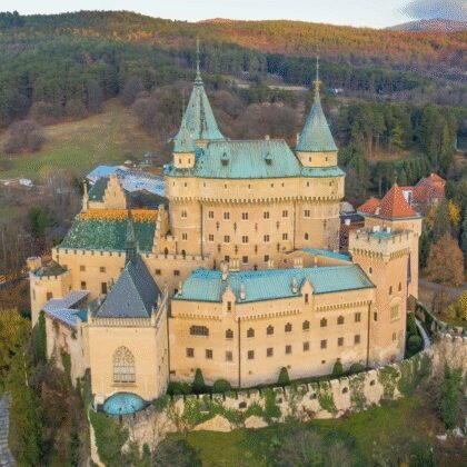 Aerial view of Bojnice Castle surrounded by autumn forests in Slovakia, medieval architecture is visible.
