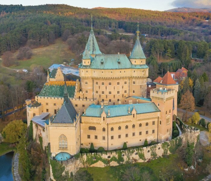 Aerial view of Bojnice Castle surrounded by autumn forests in Slovakia, medieval architecture is visible.