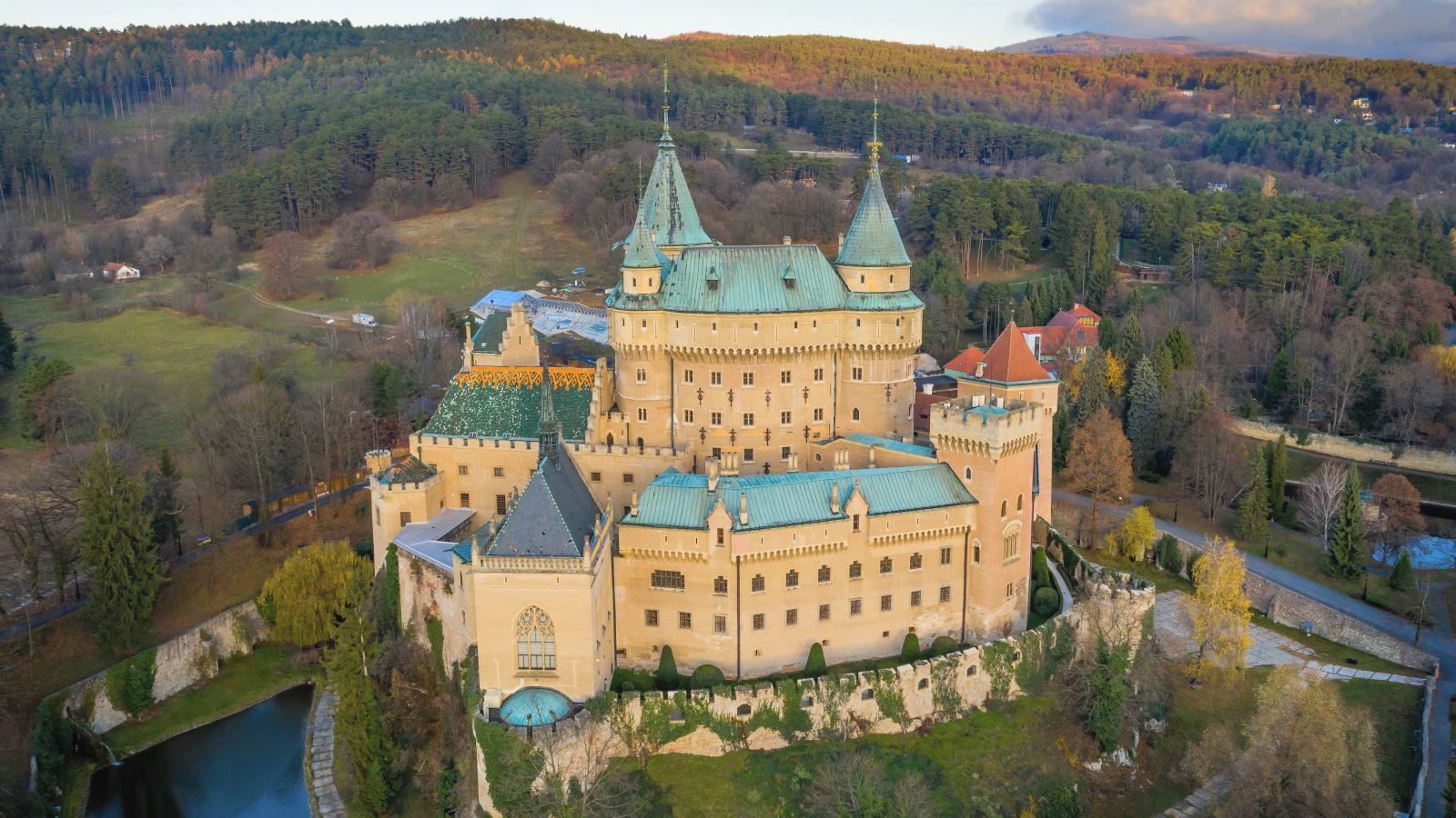 Aerial view of Bojnice Castle surrounded by autumn forests in Slovakia, medieval architecture is visible.