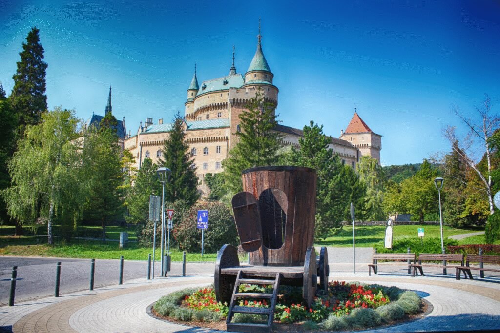 Bojnice Castle in Slovakia with lush greenery and a wooden sculpture in front