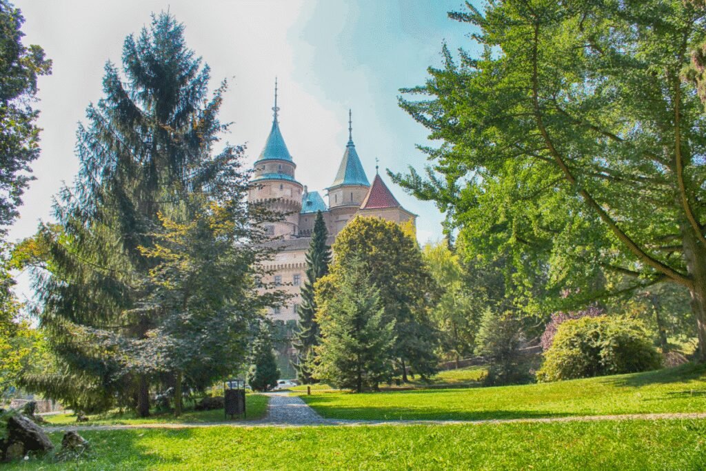 Bojnice Castle in Slovakia framed by lush green trees and a sunny park.
