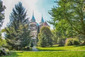 Bojnice Castle in Slovakia framed by lush green trees and a sunny park.