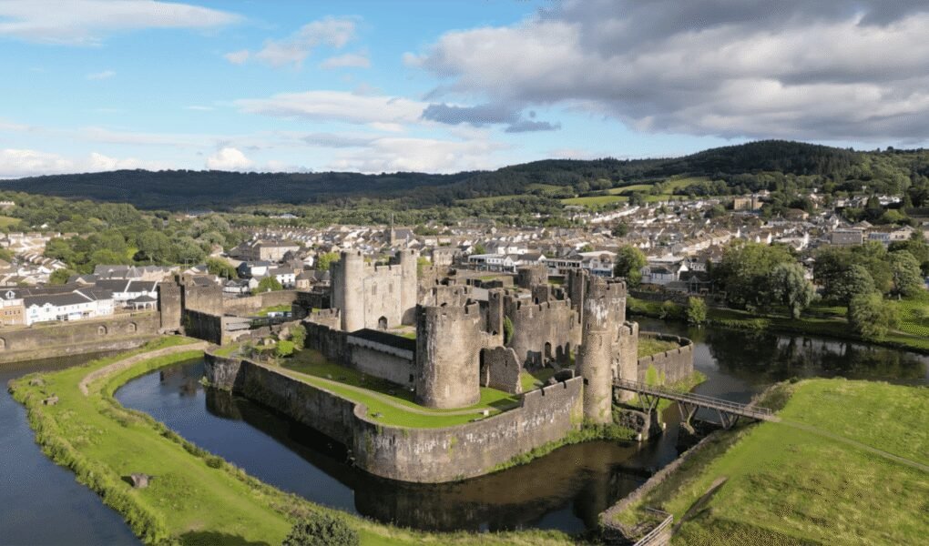 Caerphilly Castle surrounded by moat and Welsh hills, showcasing medieval architecture.