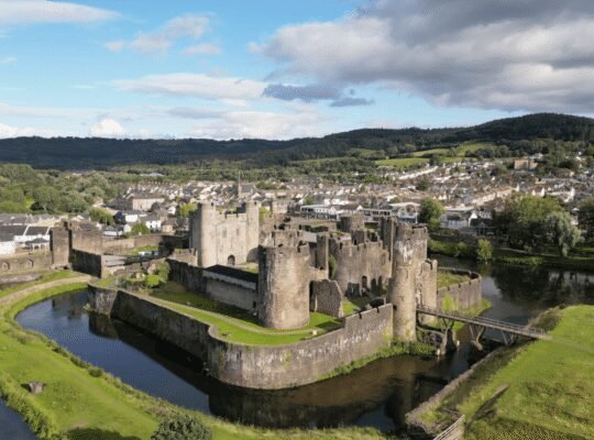 Caerphilly Castle surrounded by moat and Welsh hills, showcasing medieval architecture.