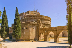 Castel Sant'Angelo rises behind ancient Roman arches under a clear blue sky in Rome.