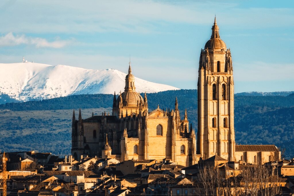 Segovia Cathedral with snowy mountains in the background, illuminated by sunset light.