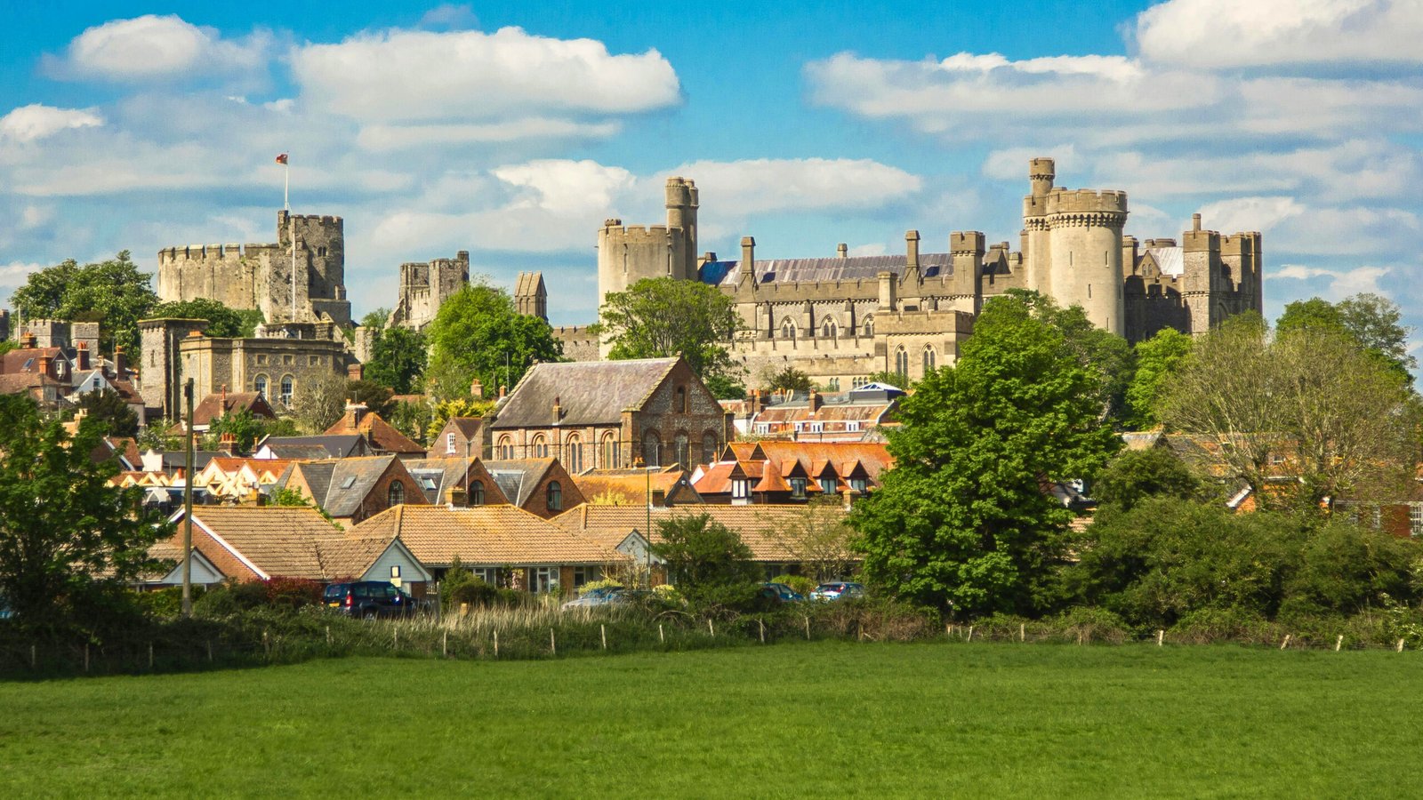 Panoramic view of Arundel Castle above rooftops and green fields under blue sky in West Sussex.