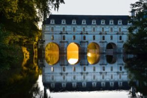 Sunset at Château de Chenonceau, arches reflected on calm river waters.
