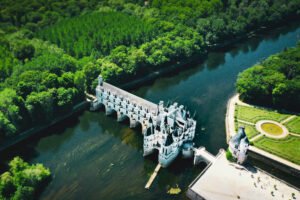 Aerial photo of Chenonceau Castle above the Cher River in the Loire Valley, surrounded by lush forest.