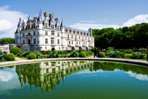 Beautiful Chenonceau Castle reflected in a tranquil garden pond in the Loire Valley on a sunny day.